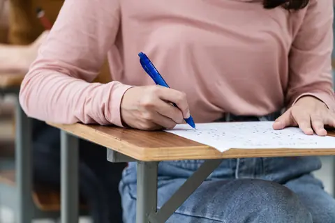 Ученица в розовом свитере пишет ответы на экзамене